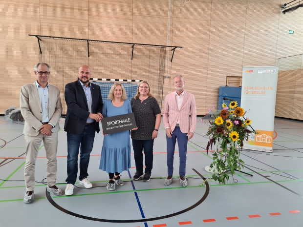 Fünf Personen stehen in einer sporthalle und halten ein Schild mit der aufschrift 