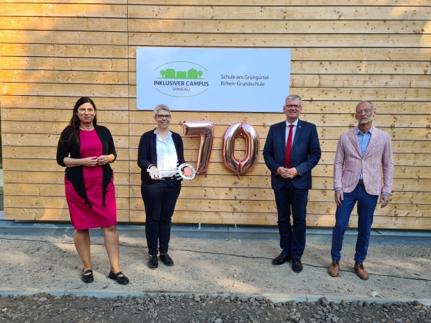Sandra Scheeres, Direktorin Anja Dudkowiak, Helmut Kleebank und Hermann Josef-Pholmann vor einer Wand aus Holz mit einem Schild 
