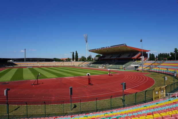 Eine Rasenfläche mit einer Laufbahn, im Hintergrund eine Tribüne